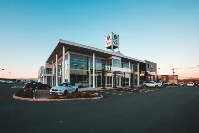 A modern BMW car dealership in a city with luxury cars and clear blue sky.