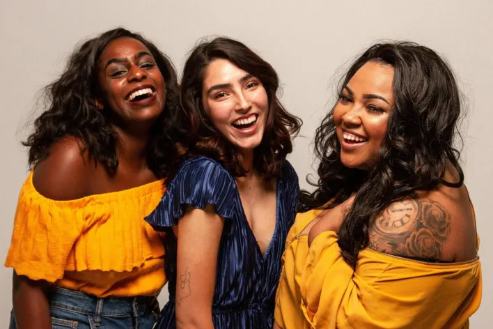 Joyful group of diverse women laughing together in bright outfits.