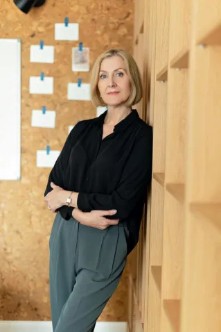 A confident mature woman stands in a modern office environment, exuding professionalism and elegance.