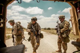 Three soldiers in camouflage gear with rifles in an outdoor military training exercise.