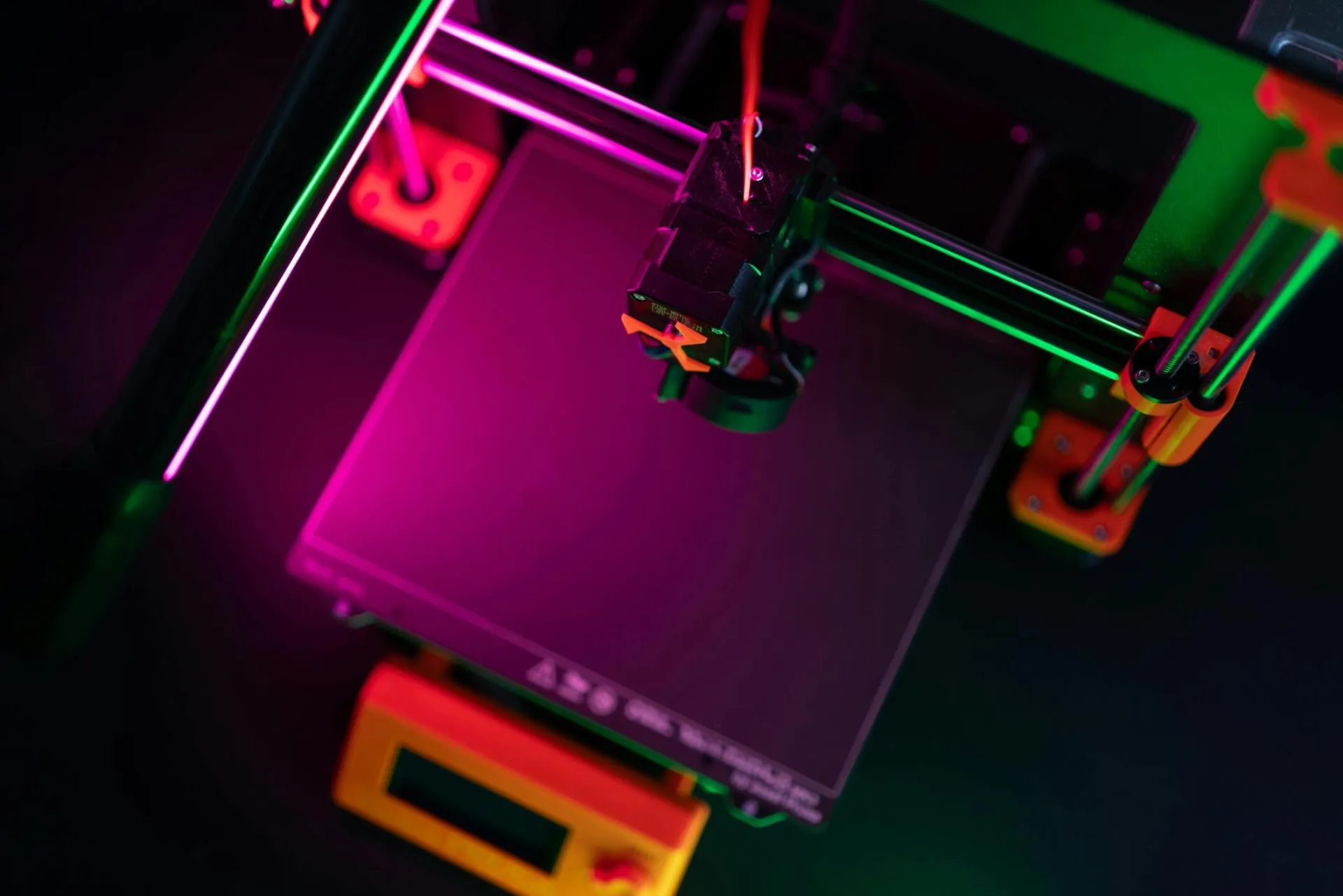 A vibrant overhead view of a 3D printer with neon lighting, emphasizing modern manufacturing.