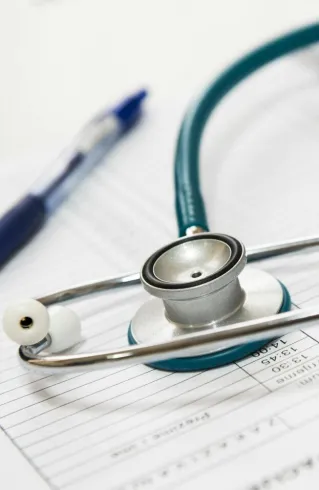 A stethoscope and pen resting on a medical report in a healthcare setting.