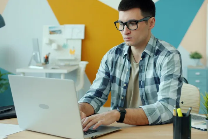 Young adult man working on a laptop in a modern office with colorful decor.