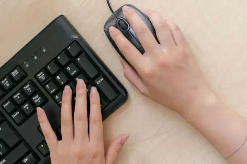 Close-up of hands on a keyboard and mouse, highlighting office work setup.