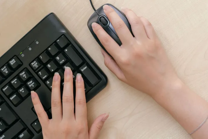 Close-up of hands on a keyboard and mouse, highlighting office work setup.
