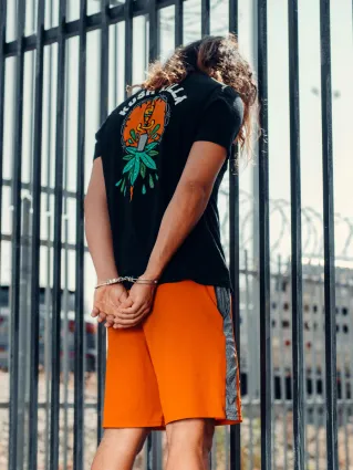 Back view of a handcuffed individual near prison bars under daylight.