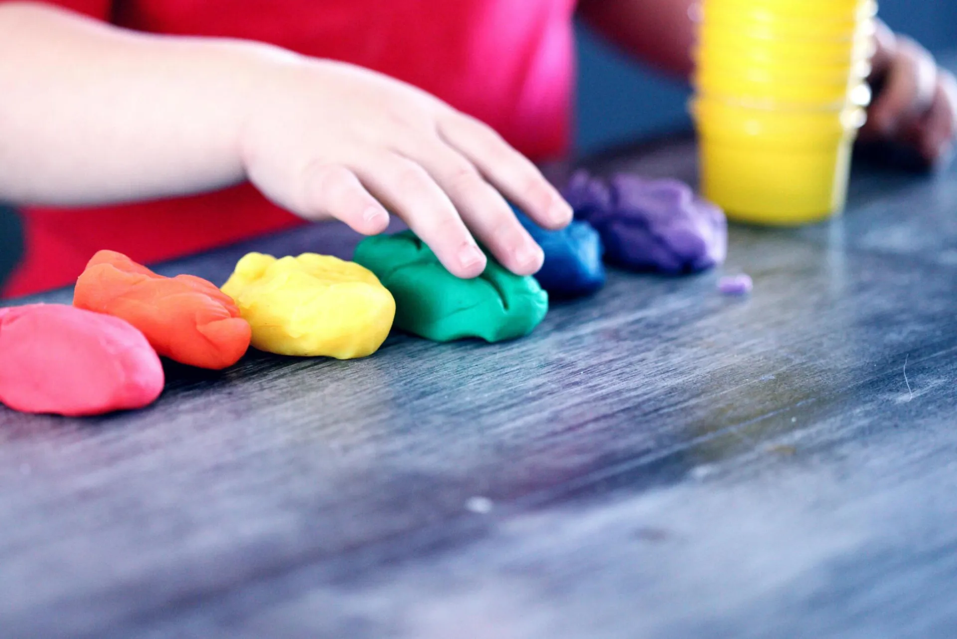 A young child with rainbow-colored modeling clay and stacking cups on a table indoors.