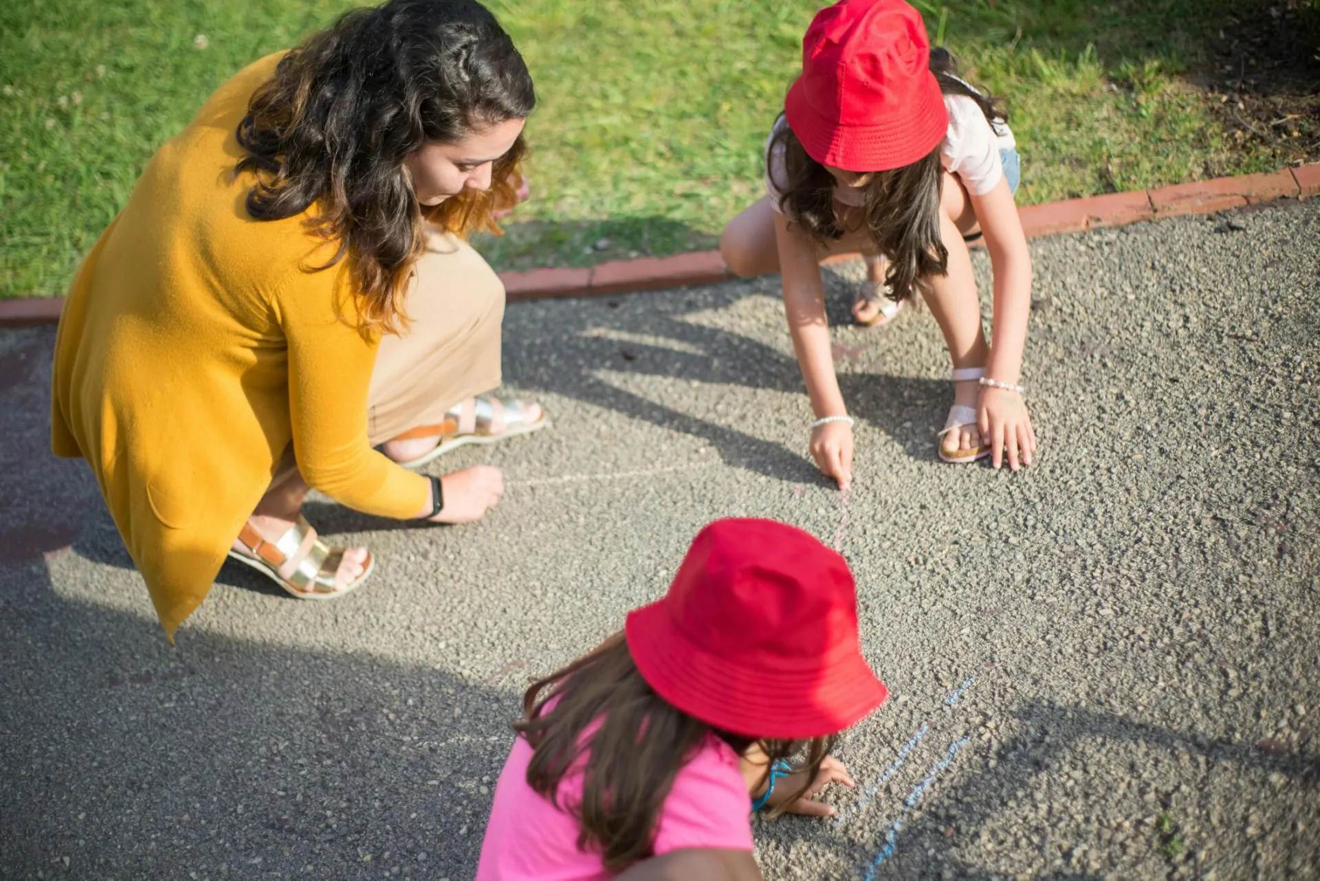 A nanny and two children drawing together on the pavement outdoors in Portugal.