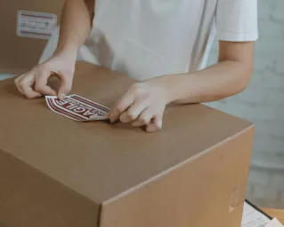 Woman preparing shipment by applying a 'fragile' sticker on a cardboard box in a warehouse.
