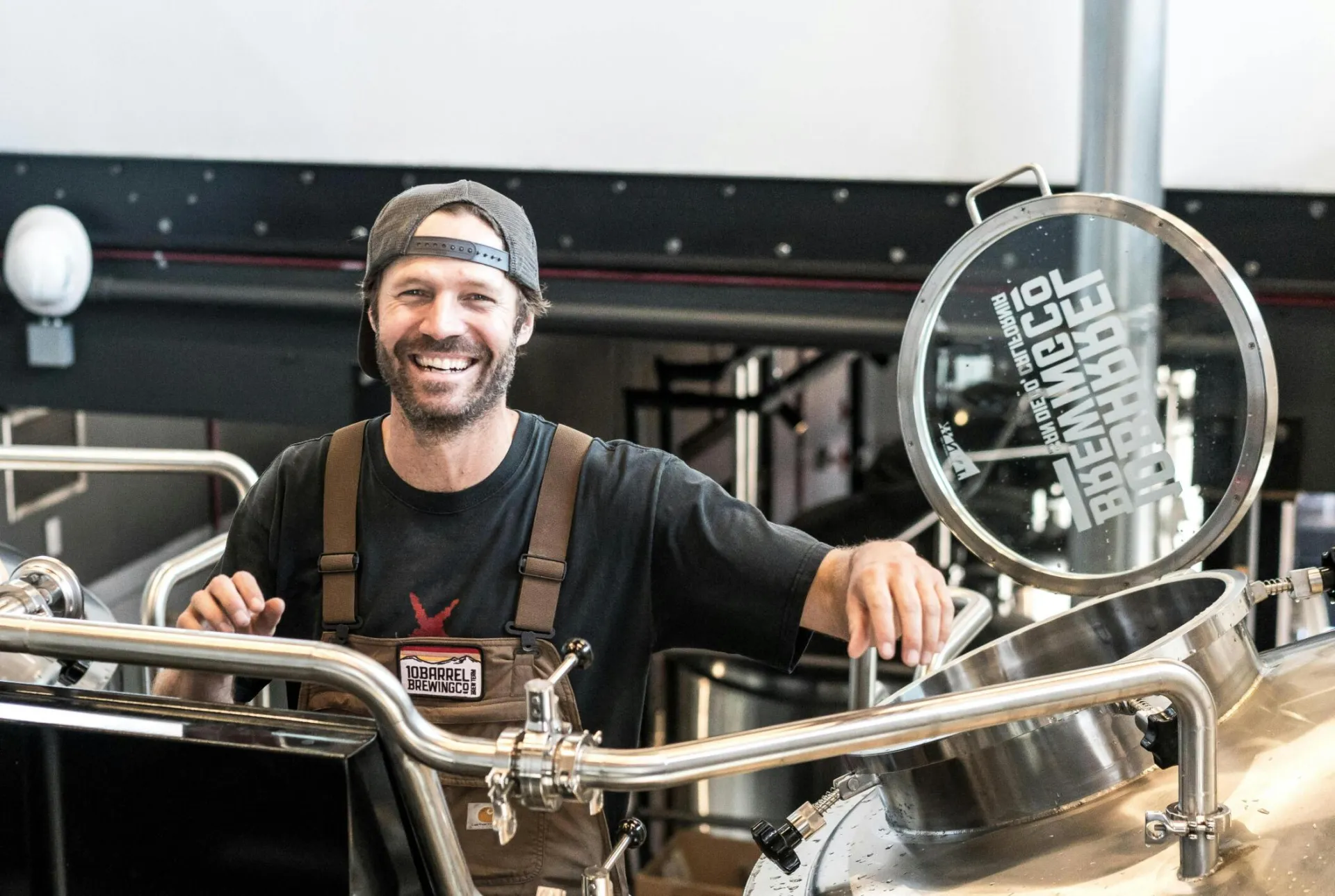 Happy brewer in a craft brewery standing near stainless steel equipment.
