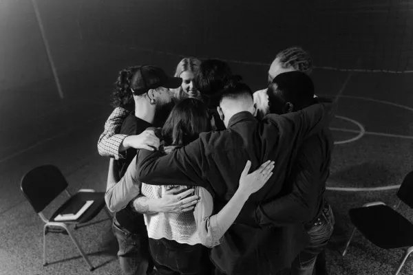 A diverse group in a supportive embrace during a meeting, symbolizing unity and connection.