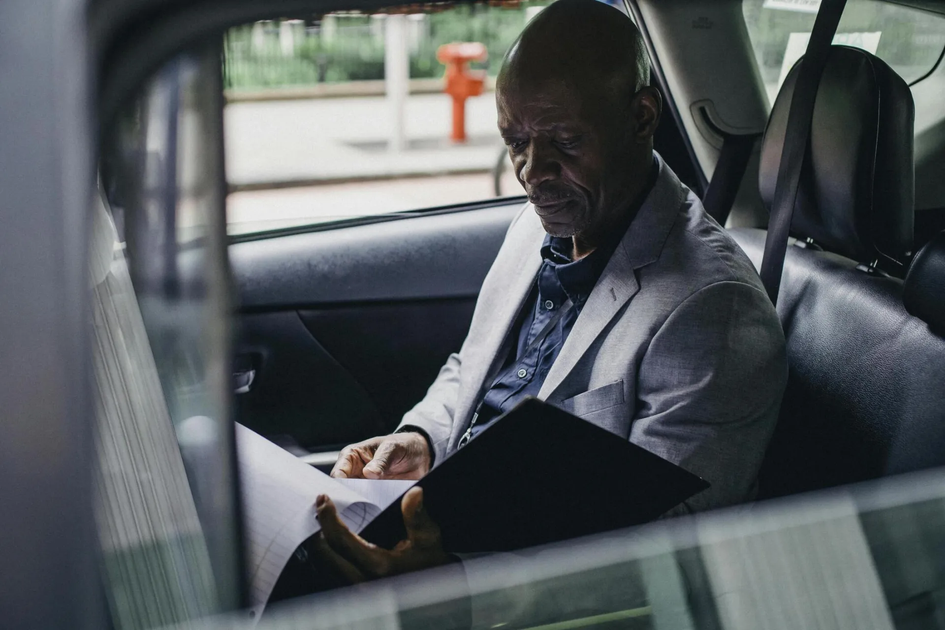 Side view serious African American businessman in formal clothes sitting in car back seat and reading documents