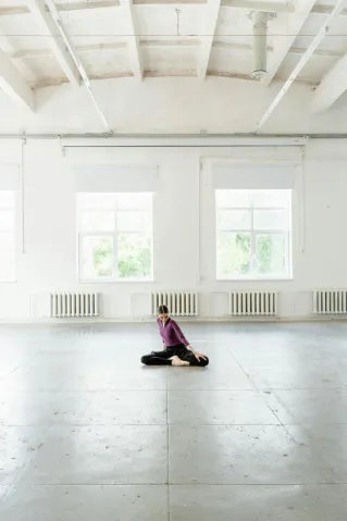A dancer performs a pose in a spacious, sunlit ballet studio.