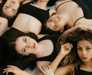 Artistic photo of a group of women with striking makeup and black outfits, lying together.