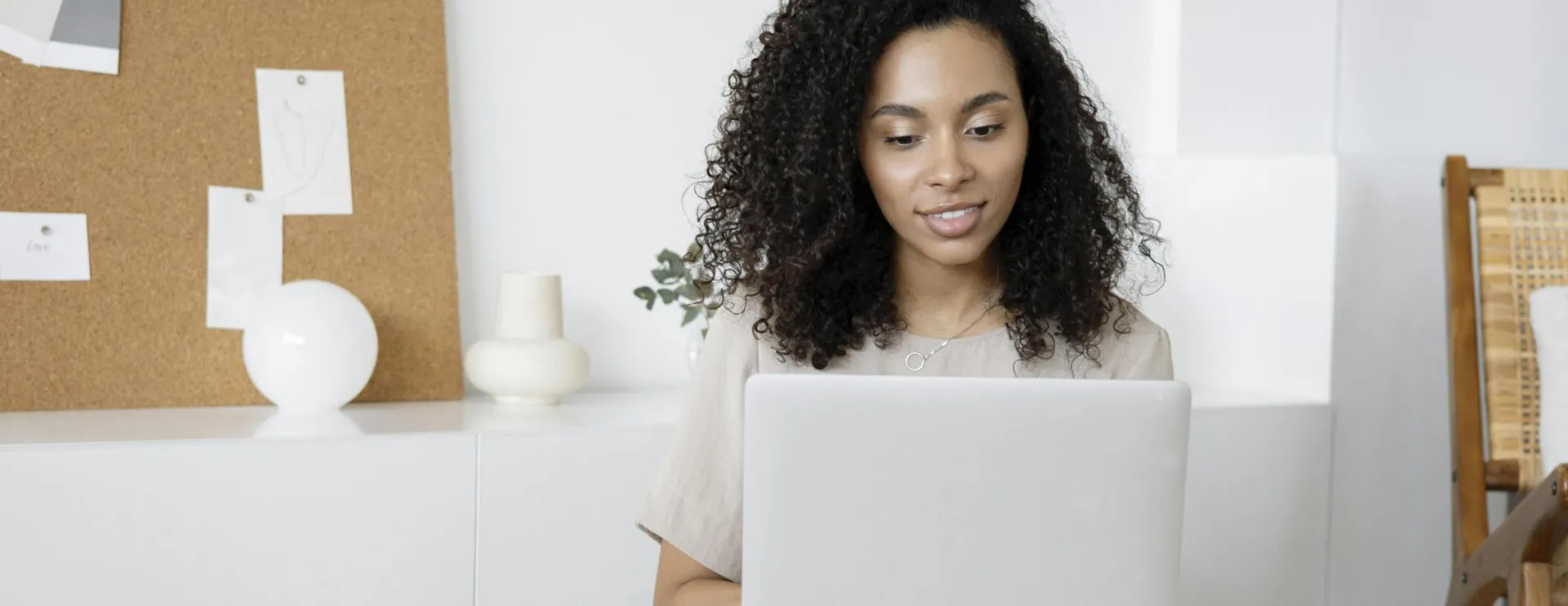 Young woman with curly hair working on her laptop in a cozy home setting, exuding confidence and focus.