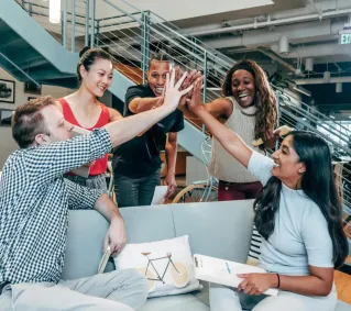 A multicultural office team high-fiving and celebrating a successful collaboration.