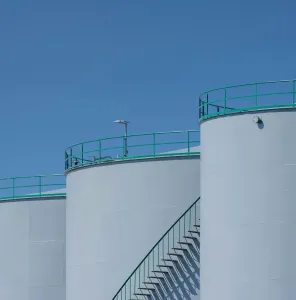 Large industrial storage tanks with green railings against a clear blue sky.