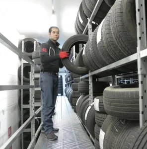Mechanic places a tire on a rack in an indoor warehouse storage facility.