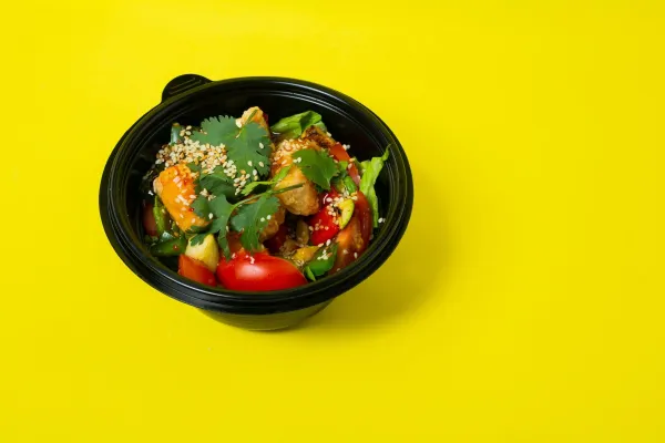 From above of delicious healthy salad consisting of various vegetables in plastic bowl placed on bright yellow background