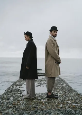 Couple standing back-to-back on a rocky pier by the sea, evoking themes of isolation and contemplation.
