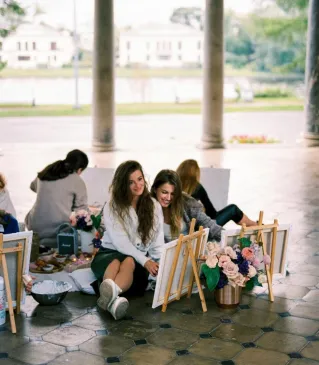 A group of women enjoying an art session in an outdoor pavilion with columns.