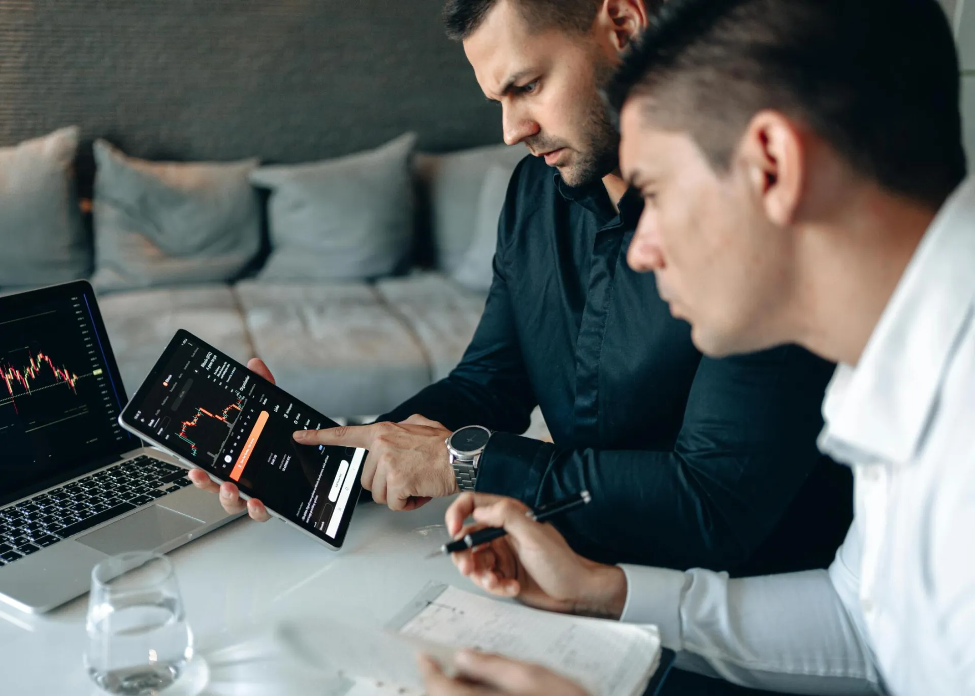 Two business professionals using a laptop and tablet to analyze online trading data indoors.
