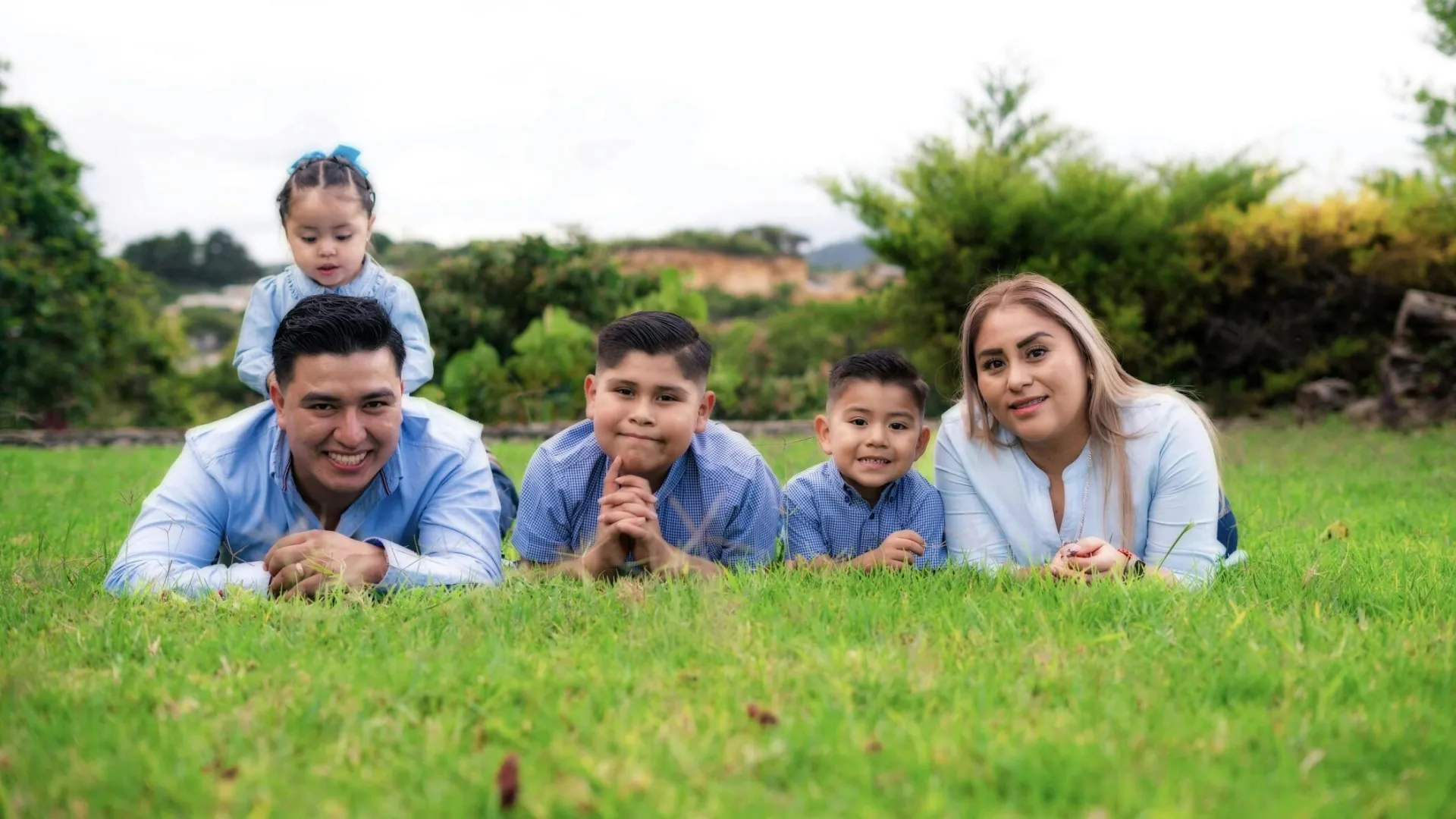Smiling family of five poses together on lush green grass, showcasing bonding and happiness.
