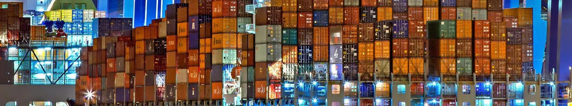 A brightly lit cargo ship at Hamburg harbor with stacked containers and a tugboat.