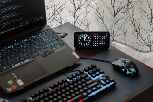A modern workspace featuring a laptop, digital clock, gaming mouse, and keyboard, ideal for work and tech enthusiasts.