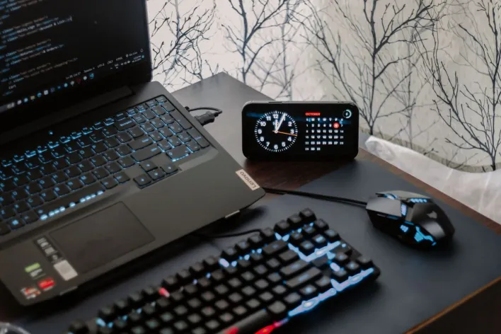 A modern workspace featuring a laptop, digital clock, gaming mouse, and keyboard, ideal for work and tech enthusiasts.