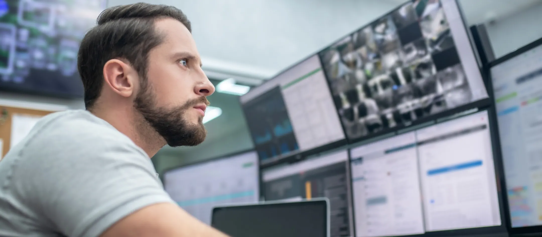 A man looks very focused and is surrounded by monitors displaying camera feeds and messaging software