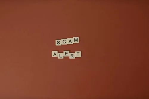 Scrabble tiles spelling Scam Alert on a brown surface indicating caution.