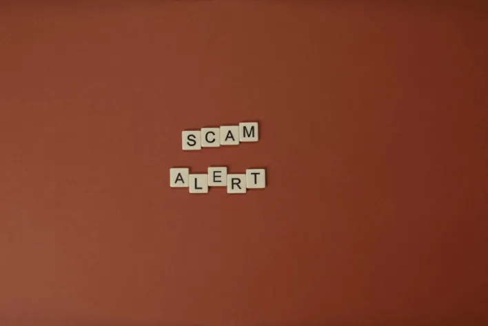 Scrabble tiles spelling Scam Alert on a brown surface indicating caution.