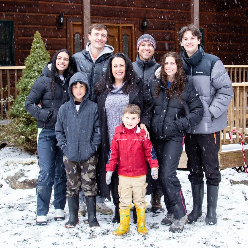 large family photo in front of a cabin while snow falls peacefully