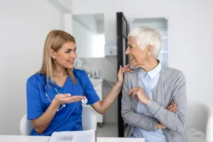 Young doctor kindly discussing with older woman with her hand resting on her shoulder
