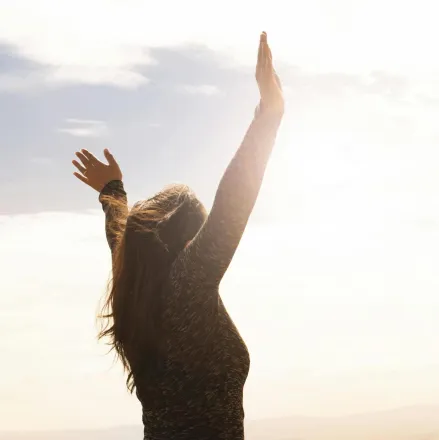 A woman with raised arms enjoying the bright open sky in a serene outdoor setting.