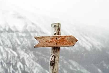 A wooden arrow signpost points the way amidst a snowy mountain landscape.