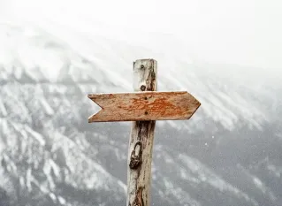 A wooden arrow signpost points the way amidst a snowy mountain landscape.