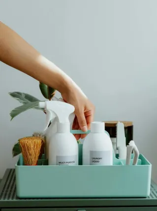 Hand arranging cleaning products in a tidy organizer, promoting cleanliness and order.