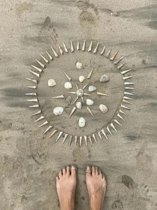 Footsteps lead to a creative seashell mandala on a sandy beach, embodying tranquility.