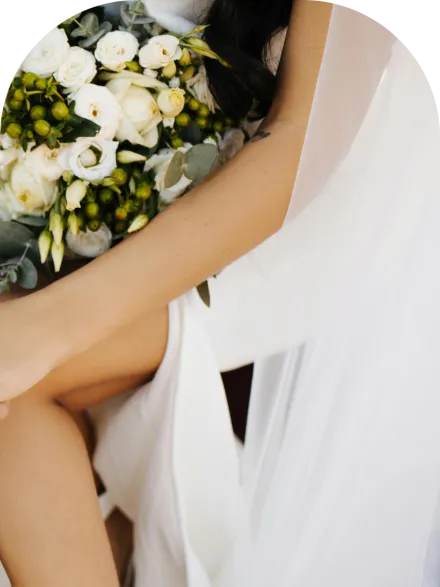 Close-up of a floral necklace adorning a bride in a strapless white wedding dress outdoors.
