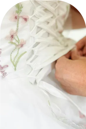 Delicate hands tying the back of a floral wedding dress, symbolizing care and elegance.