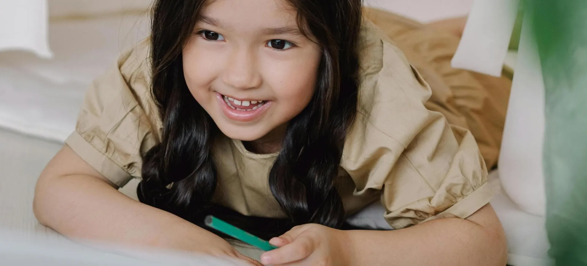 Cute Asian girl smiling while using a laptop for her online class, showcasing joyful learning.