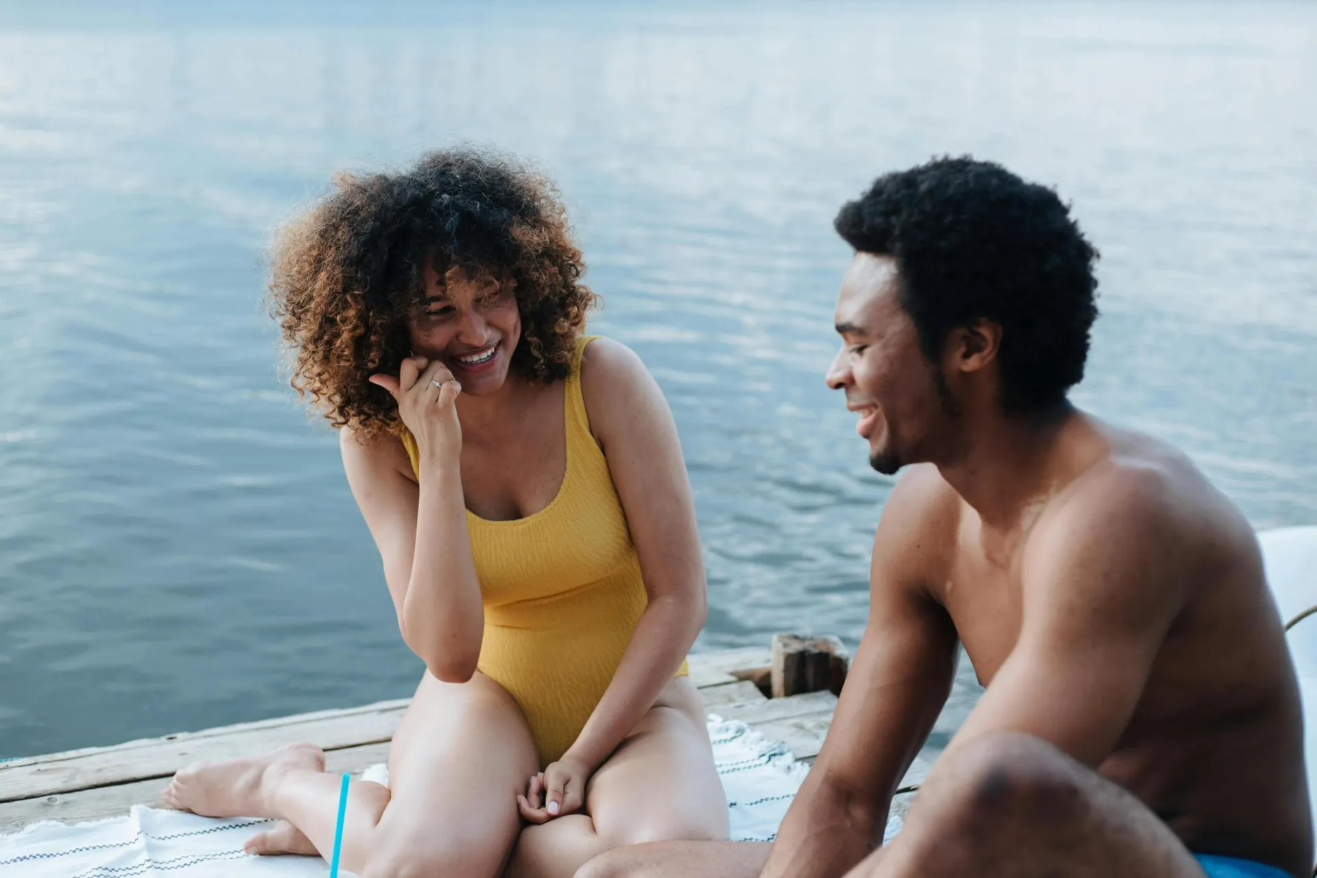 Two friends laughing and enjoying a sunny day sitting on a oceanside dock.