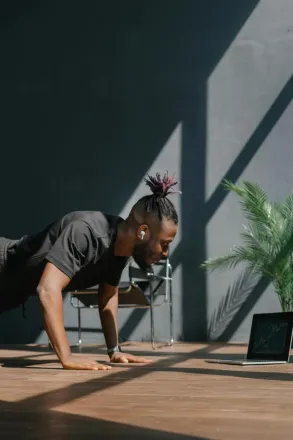 An adult man doing push-ups indoors, guided by a laptop. Fitness and technology merge.