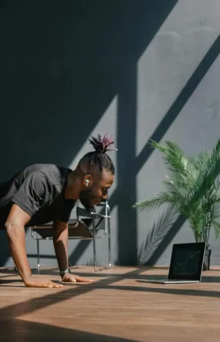 An adult man doing push-ups indoors, guided by a laptop. Fitness and technology merge.