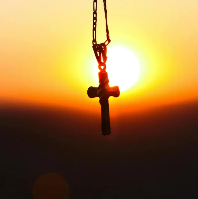 A cross pendant silhouetted against a vibrant sunset, symbolizing faith and peace.