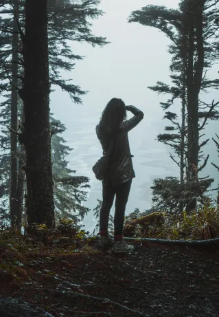 Silhouette of a woman standing in a misty Oregon forest amidst tall trees, capturing the serene atmosphere.