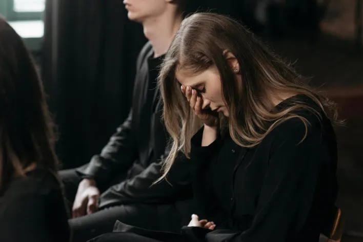 A woman in black clothing expresses sorrow at a funeral, reflecting on loss.