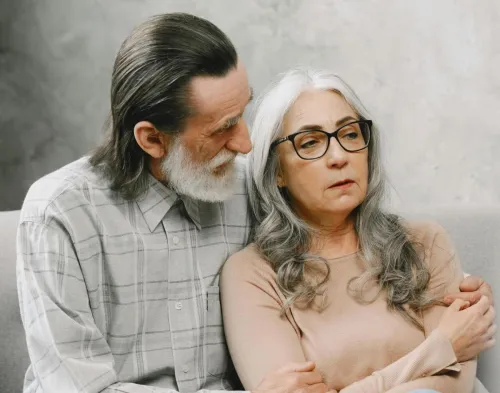 Elderly couple sitting closely, expressing comfort and support in a cozy living room setting.